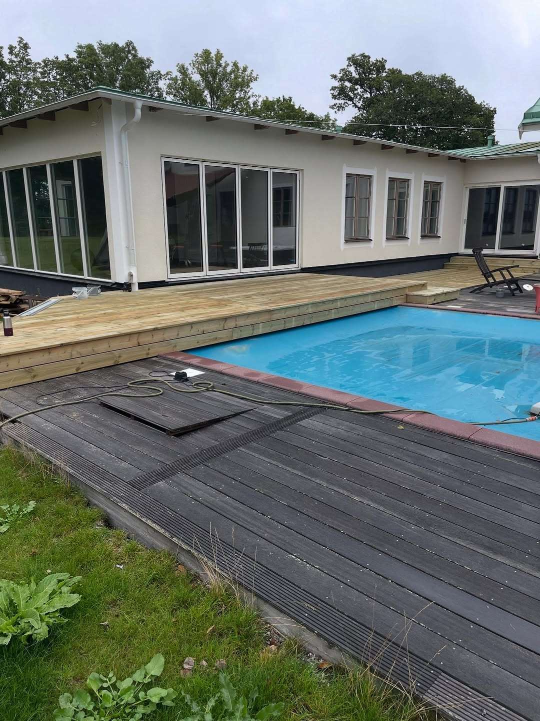 Nylagt trädäck som ansluter mot ett vitputsat hus och en pool.