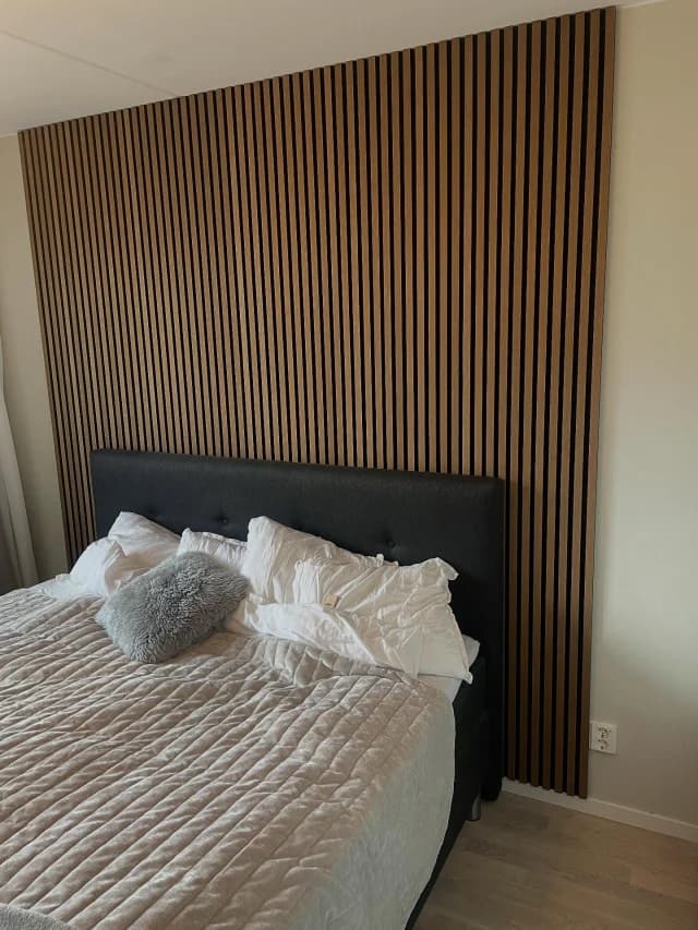 Vägg klädd med akustikpanel i ek från golv till tak bakom en säng.