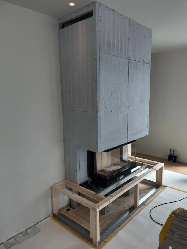 Kamin inbyggd i en inklädd skiva från golv till tak, uppallad på en tillfällig träställning.