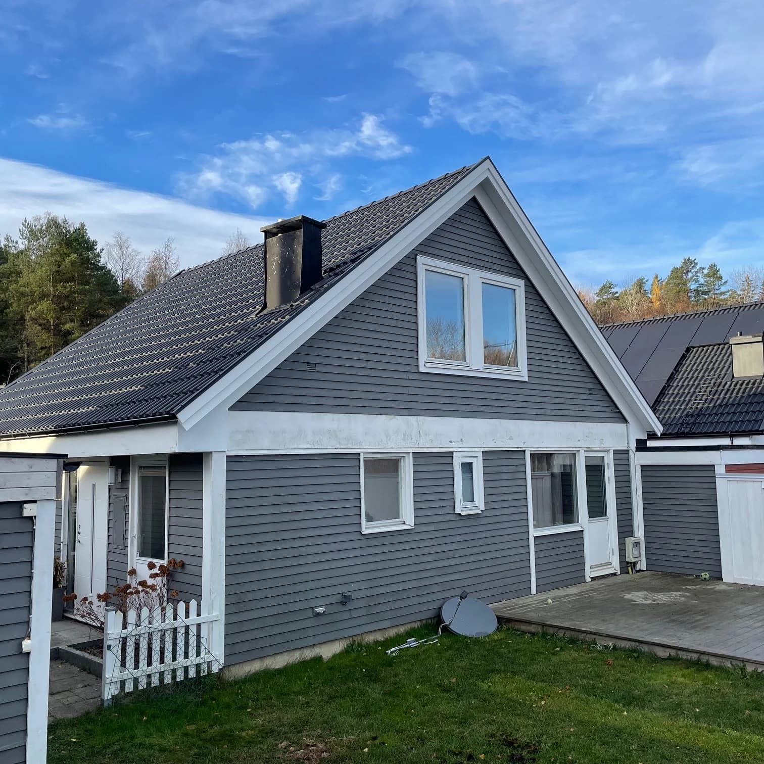 Gaveln på ett grått trähus med tegeltak och vitmålade vindskivor.